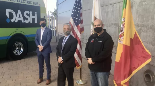 Three men standing in front of the US, State of California and City of Los Angeles flags.