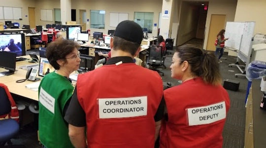 Three individuals standing while wearing vests.