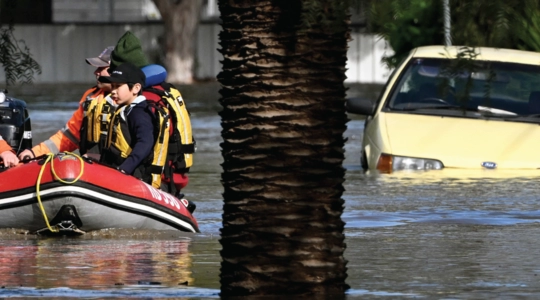 Photo of a rescue scene in a flooded area showing a submerged car and victims being taken from the scene in a raft.