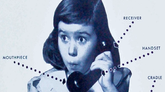 Old photo of a girl talking on a mid-2oth centure rotary dial phone.