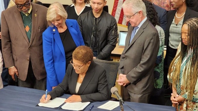 Photo of Mayor Karen Bass of LA City seated at a table signing an emergency declaration at the EOC, December 11, 2022. She is surrounded by other City and County elected officials.