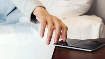 Image of a person's hand, reaching for a phone on a bedside table.