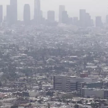 Shows a long-distance photo of the Los Angeles downtown skyline with very smoggy skies.