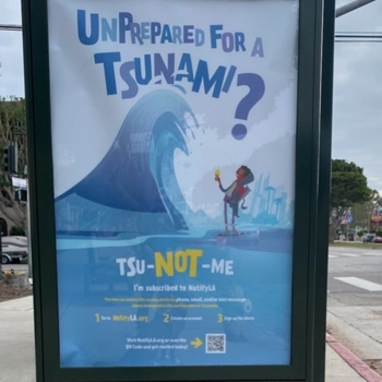 Photo of a bus-shelter poster for the EMD tsunami awareness campaign launched in May 2023. Includes a drawing of a cartoon figure standing under a massive ocean wave, with the caption "unprepared for a Tsunami? TSu-NOT-me. NotifyLA,org. 